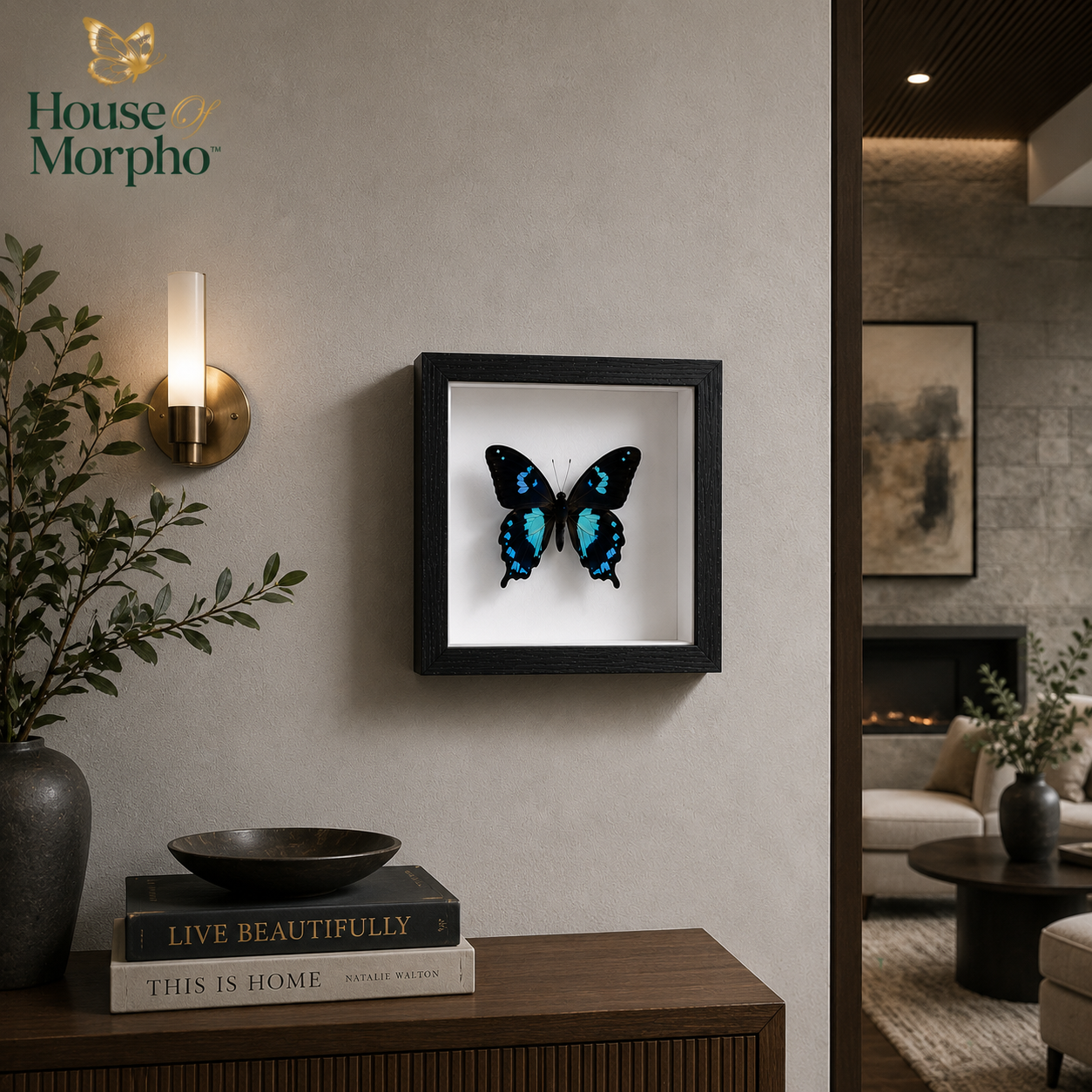 A framed butterfly wall art piece hangs on a beige wall in a styled interior. The product appears to be a black square frame containing a preserved butterfly with vivid blue, black, and white coloring on a white insert.